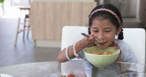 Young Girl Eating Cereal at Home Kitchen Table