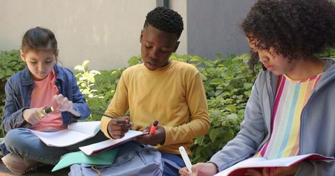 Teenagers studying together on campus courtyard sharing notes and highlighters