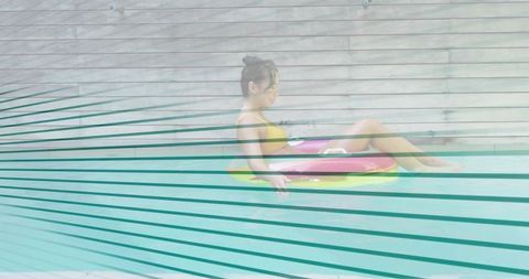 Floating woman in yellow bikini on pink inflatable ring in turquoise pool with slats