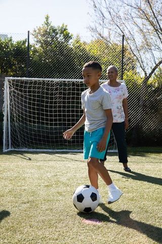 Boy Playing Soccer in Backyard with Grandmother Watching