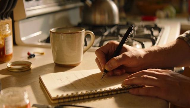 Writing in spiral notebook with coffee mug on warm kitchen counter during morning light