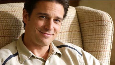 Relaxed smiling man lounging on patterned armchair in cozy home interior portrait