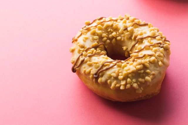This image features a close-up of a donut topped with sprinkles, set against a vibrant pink background. Ideal for use in marketing materials for bakeries, cafes, or dessert shops. Can also be used in articles or blogs discussing sweet treats, unhealthy eating habits, or food photography.