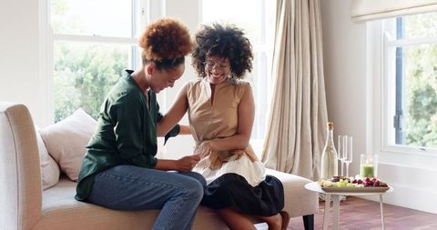 African American friends sharing surprise card on cozy sunlit sofa, celebrating together