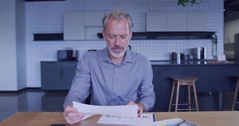 Mature business analyst reviewing financial charts in modern office kitchen