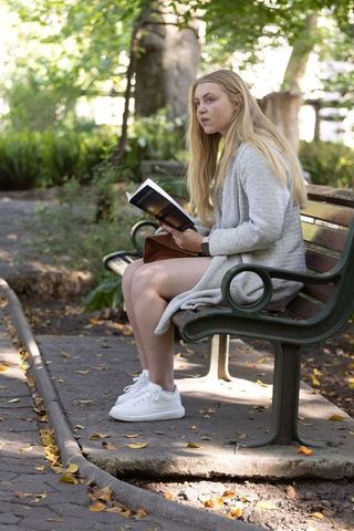 Young woman reading on park bench wearing cozy cardigan in dappled sunlight