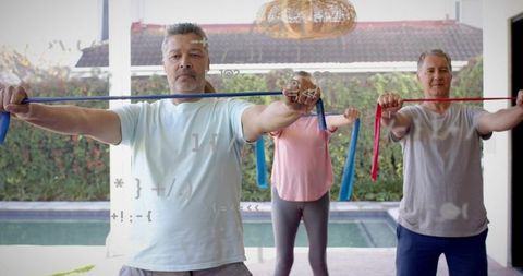 Mature adults exercising with resistance bands on backyard patio by pool
