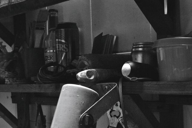 Black and white close-up of organized workbench in workshop, featuring various tools and paint supplies. Potential use for themes related to DIY projects, workshops, craftsmanship, or industrial workplaces. Suitable for home improvement blogs, articles on organization, or creative design projects.
