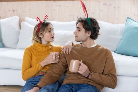 Young couple celebrating holiday with festive headbands and warm drinks
