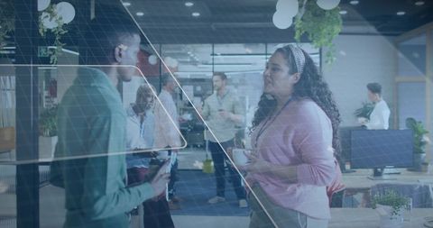Colleagues chatting and sharing coffee in modern open-plan office with glass partitions and plants