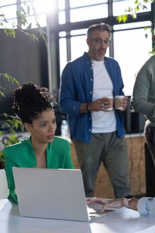 Sunlit coworking scene showing diverse professionals collaborating around laptop workstation