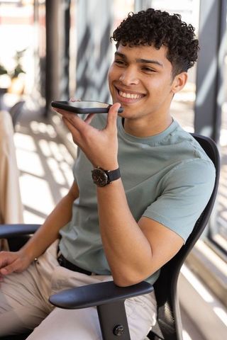 Young professional using smartphone for voice command in sunlit office
