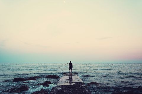 Solitary Figure Walking on Pebble Pathway by Serene Ocean
