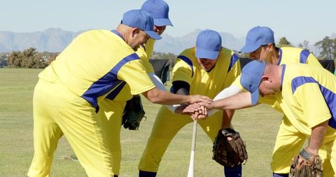 Baseball teammates stacking hands over bat in pregame huddle on grassy field