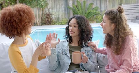 Three Friends Chatting Poolside Holding Matching Peach Mugs Casual Backyard Gathering