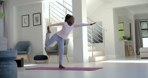 Teen girl practicing balancing yoga pose on pink mat in bright openplan living room