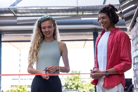 Team cutting red ribbon under glass canopy in building entrance ceremony