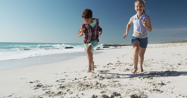 Two children enjoying running on a sandy beach under clear blue skies. Perfect for vacation and summer themes, illustrating joy and carefree childhood, advertising beach resorts or summer camps, or representing outdoor family activities.