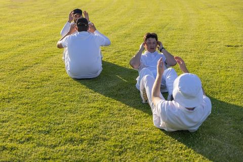 Teammates training with partner sit-ups on sunlit grass field for teamwork and camaraderie