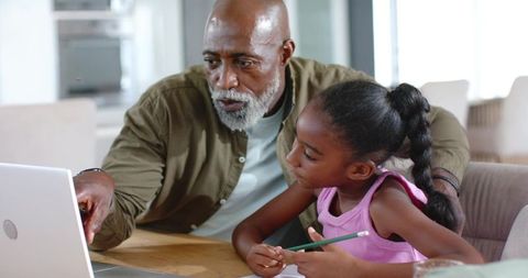 Senior african-american man helping young girl with laptop homework, mentoring and tutoring