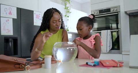 African mother guiding daughter touching fishbowl while sharing curious moment in kitchen