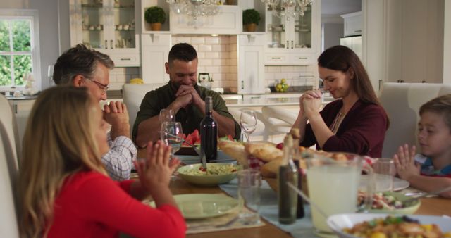 Caucasian parents, children and grandfather sitting at table for family meal saying prayers. multi-generation family enjoying time together at home.