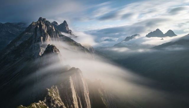 Jagged alpine ridge catching slanted sunlight with drifting fog and dramatic spires