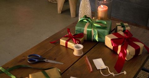 Cozy holiday gift wrapping scene on wooden table with ribboned presents and candlelight