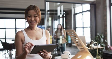 Asian Professional Holding Tablet Smiling in Modern Office Setting