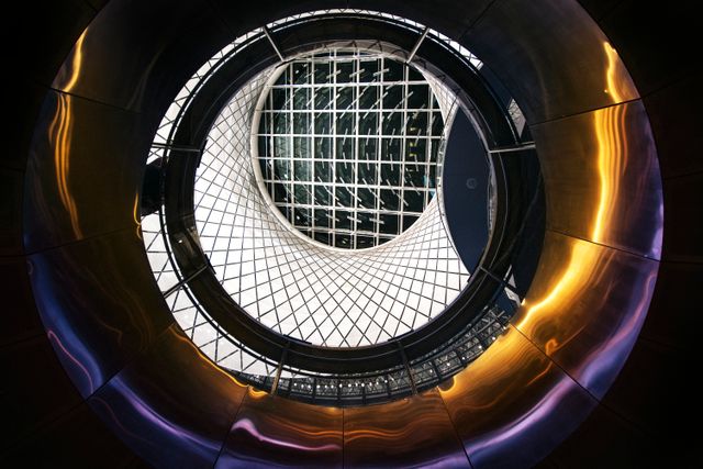 Futuristic circular architectural interior featuring a glass skylight, geometric design, and metallic reflections. The image highlights symmetry and modern structure, ideal for use in architectural magazines, design blogs, or as a digital background.