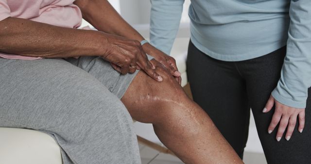 Senior person receiving knee examination from caregiver, focusing on knee area with visible scar, indicative of surgery or injury. Could be used for health-related content, medical care guidance, or physical therapy resources.