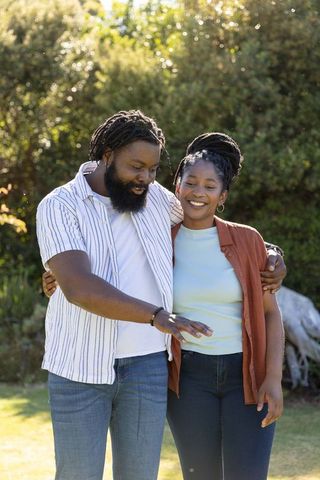 Smiling couple strolling through sunlit park, arm around and pointing toward view