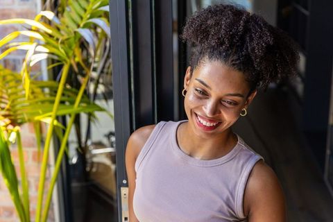 African american woman smiling in sunlit doorway with curly hair and indoor plant