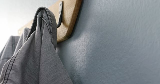 Gray shirt hanging on wooden wall hook against blue wall creates a minimalist and organized look. This image is perfect for home décor inspiration, organization tips, or interior design projects. It also works well for lifestyle or fashion articles focusing on minimalist living or wardrobe organization.