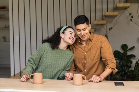 Young couple sharing cozy morning coffee at kitchen bar holding hands and smiling