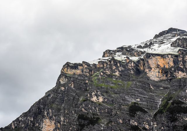Snow-capped rocky mountain peak under overcast sky with rugged terrain. Ideal for travel blogs, adventure publications, geology articles, or scenic landscape promotions.