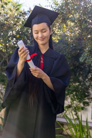 Asian female graduate holding diploma outdoors celebrating achievement