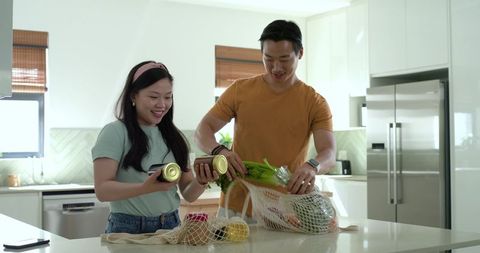 Young couple unpacking groceries and arranging fresh produce in modern kitchen