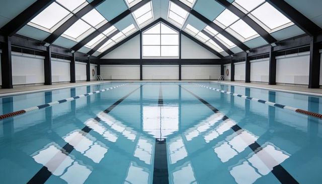 Indoor lap pool with symmetrical glass roof reflection, lane markings and daylight
