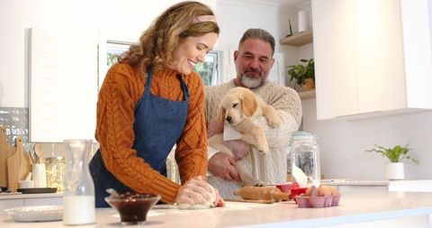 Couple baking bread together while man holding puppy in bright cozy modern kitchen