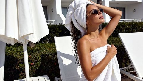 Sun-kissed woman relaxing in white towel and turban wearing sunglasses poolside resort