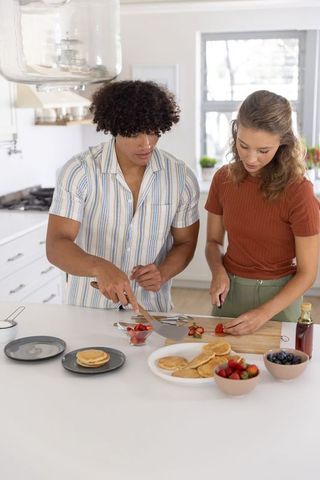 Couple preparing pancakes and slicing strawberries on bright modern kitchen island