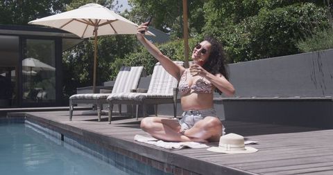 Sunlit poolside selfie african american woman sipping cocktail in bikini and shorts