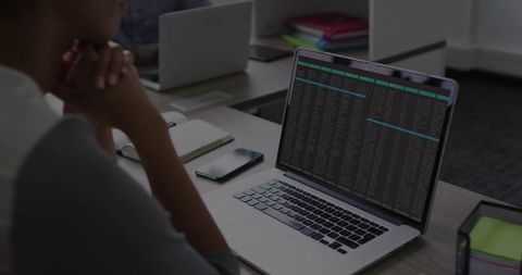 Developer Reviewing Terminal Output on Laptop in Modern Open Office with Notebook and Phone