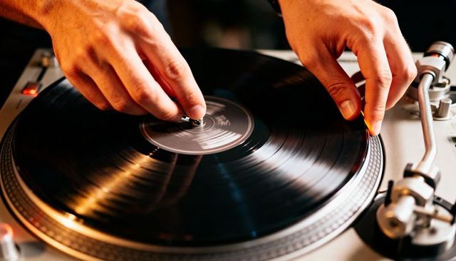 Dj hands scratching vinyl record on turntable close-up with warm lighting and reflections