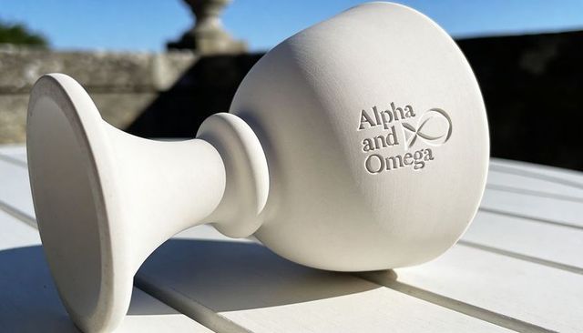 Sunlit porcelain chalice lying on slatted table casting strong shadow embossing alpha and omega