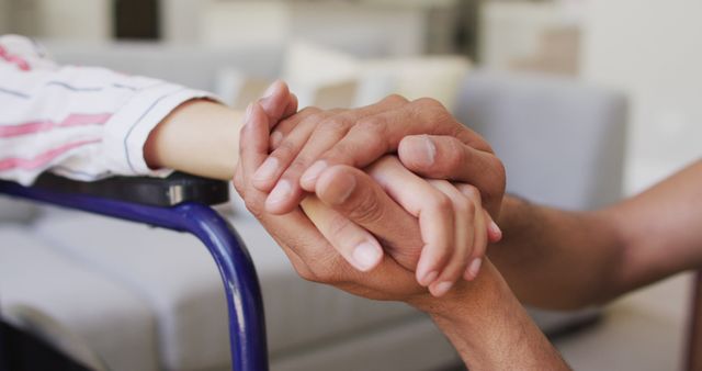 Two individuals holding hands, focusing on providing mutual support, friendship, and care. The scene includes a wheelchair, symbolizing caregiving and compassion in a home setting. Ideal for illustrating themes related to elderly care, health aid, family support, empathy for disabled individuals, and inclusive caregiving in various content such as articles, blogs, social media, and advertisements.
