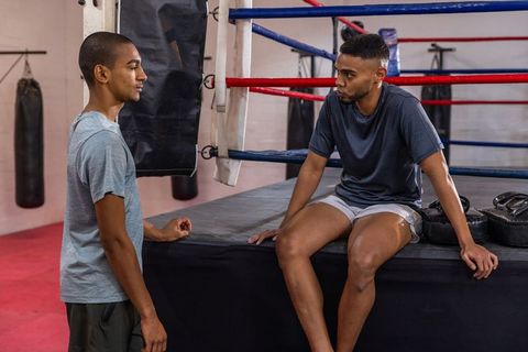 Two male boxers resting and discussing strategy on ring apron during training