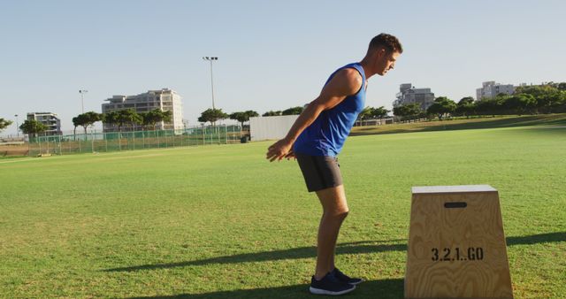 Athletic man performing box jump exercise outdoors on green field. Great for articles or promotions on outdoor fitness routines, strength training tips, and health and wellness blogs. Also ideal for sports advertising campaigns.