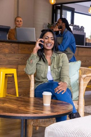 Smiling asian woman talking on smartphone in cozy modern cafe with coffee cup
